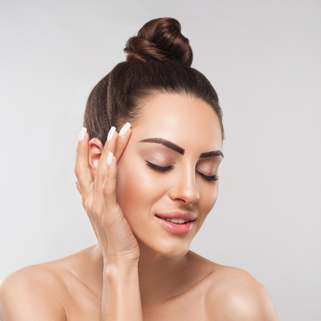 A relaxed woman with a bun holds her face